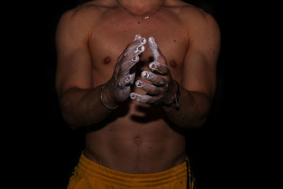 Midsection of shirtless man hands covered with talcum powder against black background