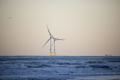 Wind turbines in sea against clear sky