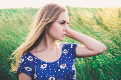 Young woman looking away while standing against grass