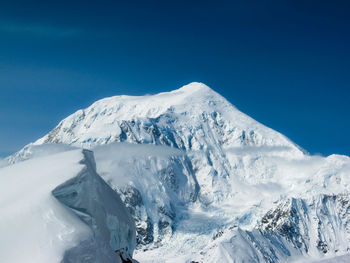 Mount foraker in the alaska range with blue sky, hanging glaciers, crevasses and low clouds