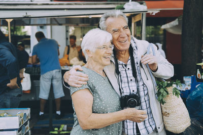Smiling senior couple with arm around standing at market in city