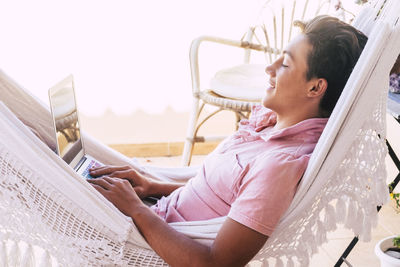 Side view of teenage boy using laptop while relaxing in hammock