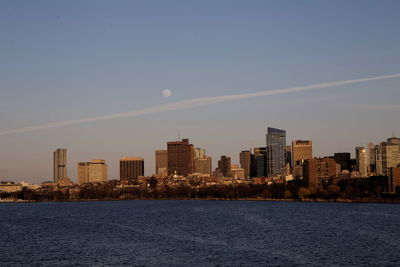 City buildings by sea against sky during sunset