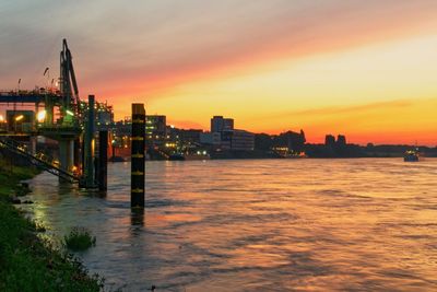 Sea by illuminated buildings against sky during sunset