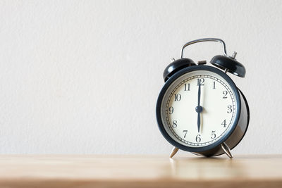Close-up of clock on table against white wall