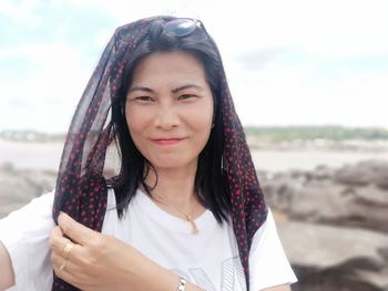 Portrait of beautiful woman wearing headscarf at beach against sky