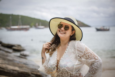 Portrait of smiling young woman wearing hat standing on beach