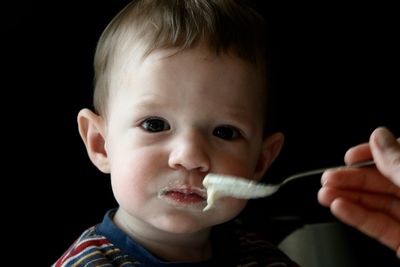 Cropped image of parent feeding baby boy against black background