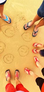 Low section of men and women standing by anthropomorphic smiley face at beach