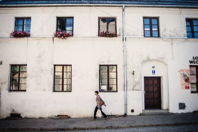 Side view full length of woman walking by building on sidewalk