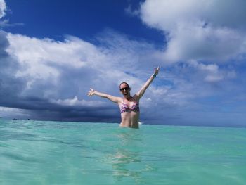 Woman with arms outstretched in sea against sky