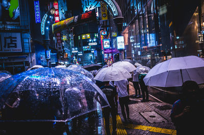 People holding umbrellas while walking on street amidst buildings at night