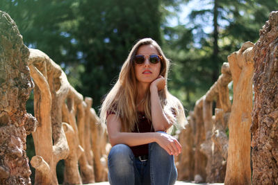 Young girl sitting casually on the path of a wooden branch bridge and looking at the camera.