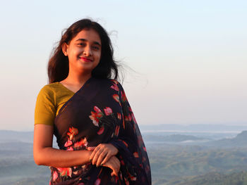 Portrait of young woman standing against sky