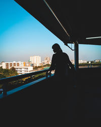 Silhouette man standing by railing in city against sky