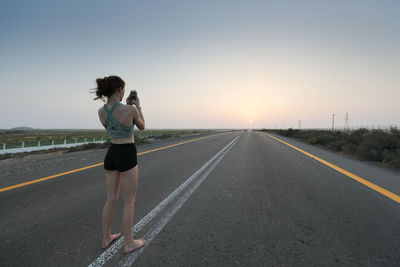 Full length of woman walking on road against clear sky during sunset