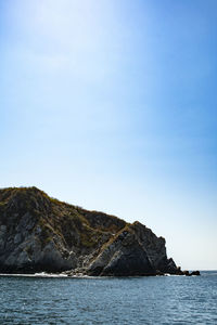 Rock formations by sea against clear blue sky