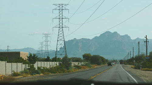 Road by electricity pylons against sky