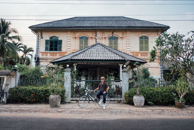 Man sitting on bicycle against building in city