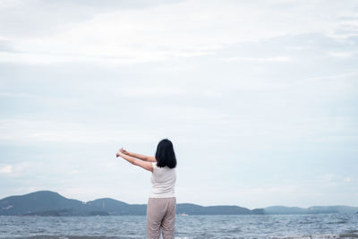 Rear view of woman standing by sea against sky