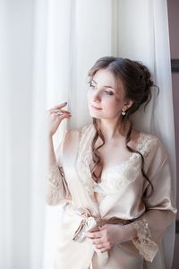 Thoughtful women in nightie standing by curtain at home