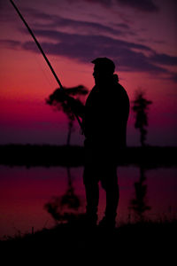 Silhouette man standing against sky during sunset and fishing