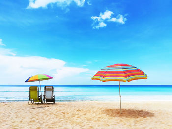 Deck chairs on beach against sky