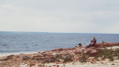 Man sitting at beach against sky