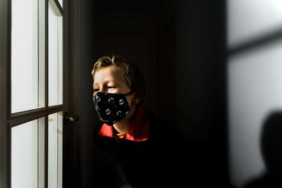 Close-up of boy wearing mask looking through window at home