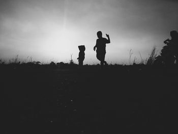 Silhouette siblings walking on field against sky