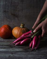 Woman holding bunch of greshly harvested radishes, pumpkins in the background.
