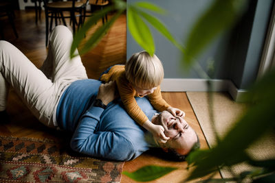 Playful daughter pinching cheerful father's cheeks on floor at home