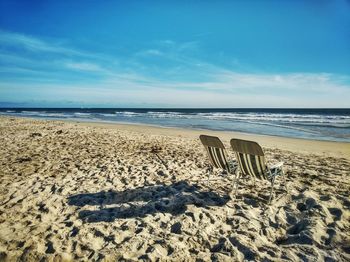 Empty chairs at beach against sky