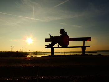 Side view of silhouette man reading book in bench against lake at sunset