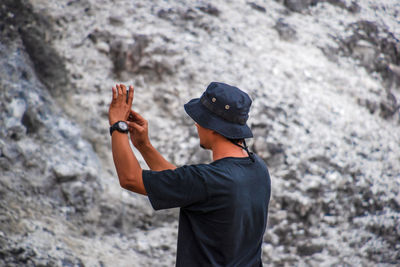 An asian man taking a picture with his cellphone on a rock, rear view 