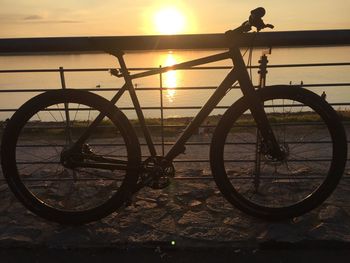 Silhouette bicycle by sea against sky during sunset
