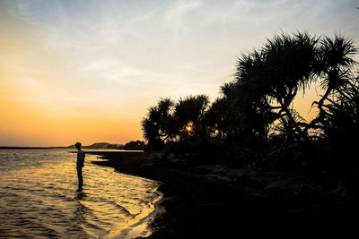 Silhouette person standing by sea against sky during sunset