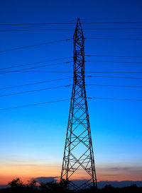 Low angle view of silhouette electricity pylon against blue sky