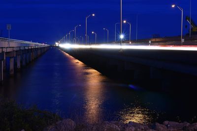 Illuminated bridge over river against sky at night