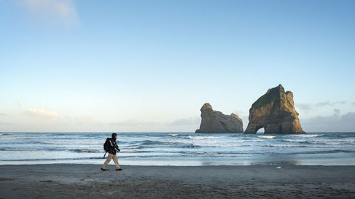 Man on rock at beach against sky