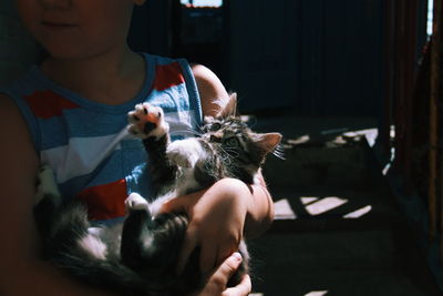 Midsection of boy carrying cat while standing at home