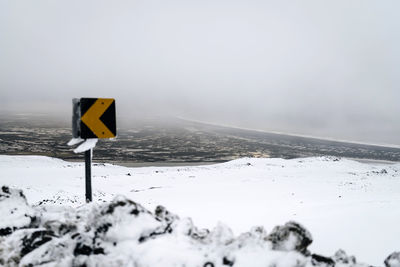 Road sign on snow covered landscape against sky