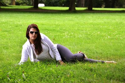 Young woman wearing sunglasses lying on grassy field at park