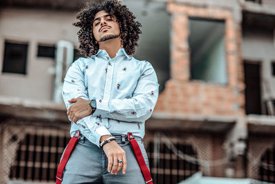 Young man looking away while standing against built structure