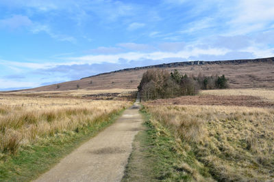 Dirt road amidst field against sky