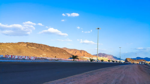 Scenic view of road by mountains against blue sky