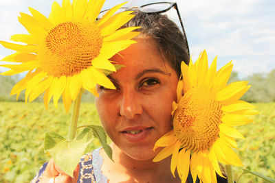 Happy nice woman hides behind yellow blooming sunflowers in summer