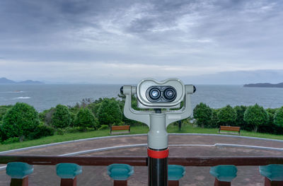 Coin-operated binoculars by sea against sky