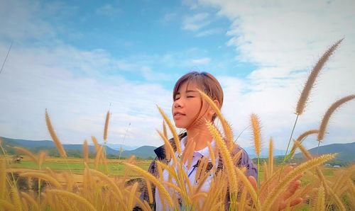 Young woman standing by crop against sky