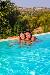 Portrait of smiling woman and daughter enjoying in swimming pool on sunny day